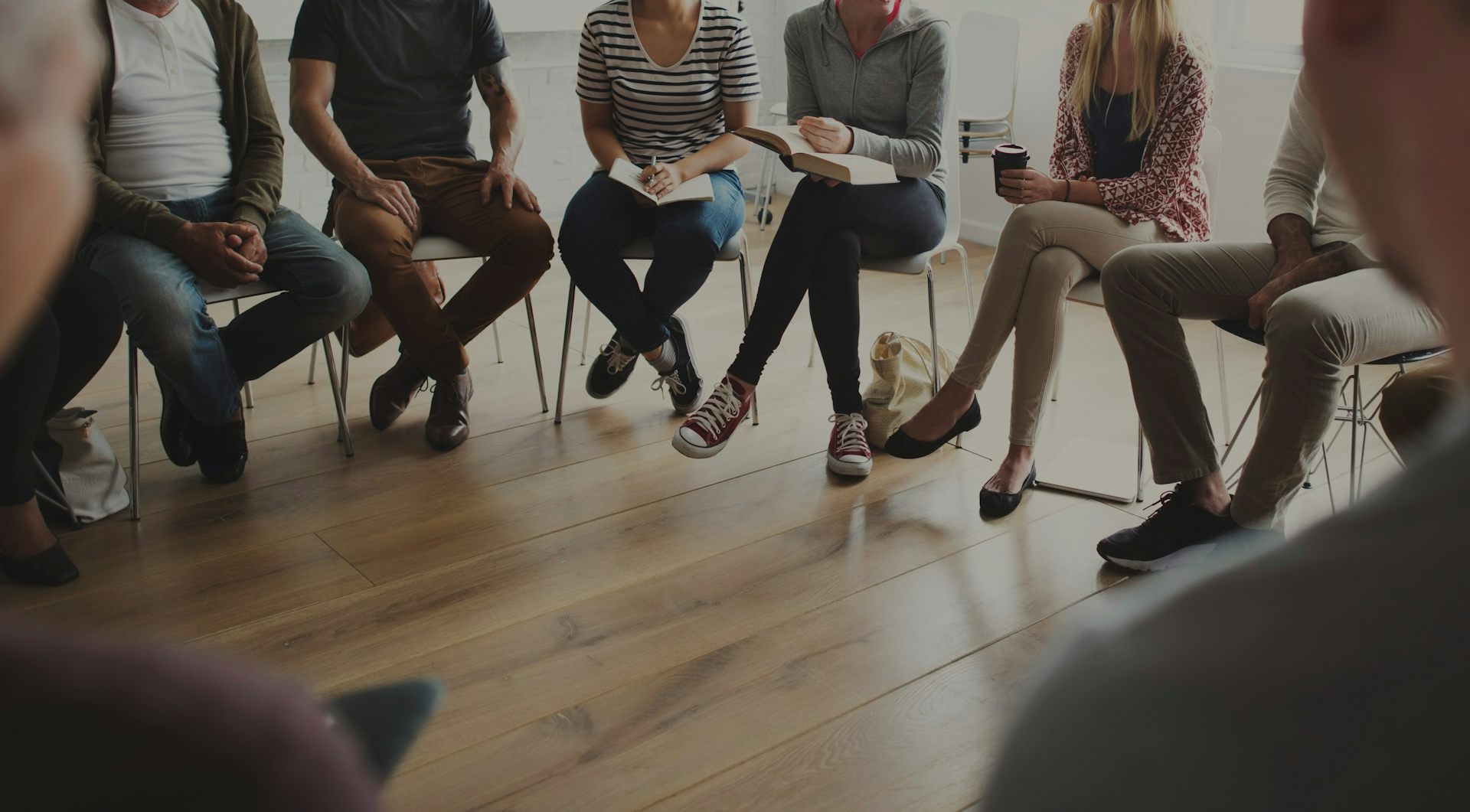 Legs of people who are sitting in a circle in a shaded room.