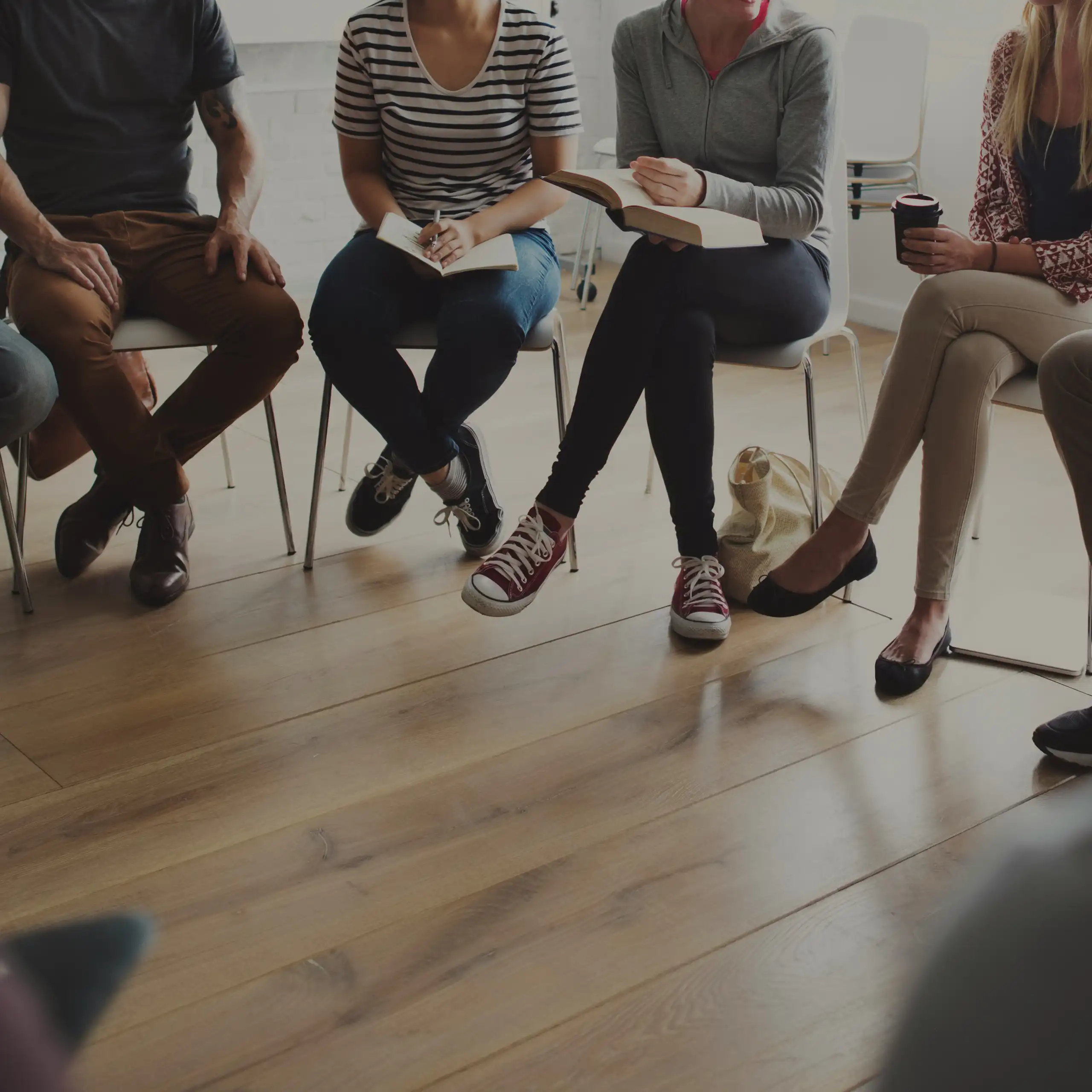 Legs of people who are sitting in a circle in a shaded room.