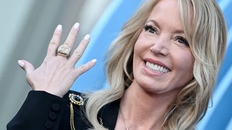 A blonde woman smiles while holding up a big ring on her middle finger.