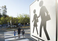 a man and two young children hold hands as they cross a street at a crosswalk