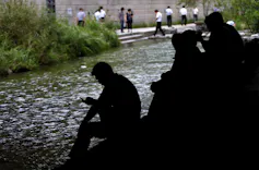 people sit by a stream of water in an urban neighborhood