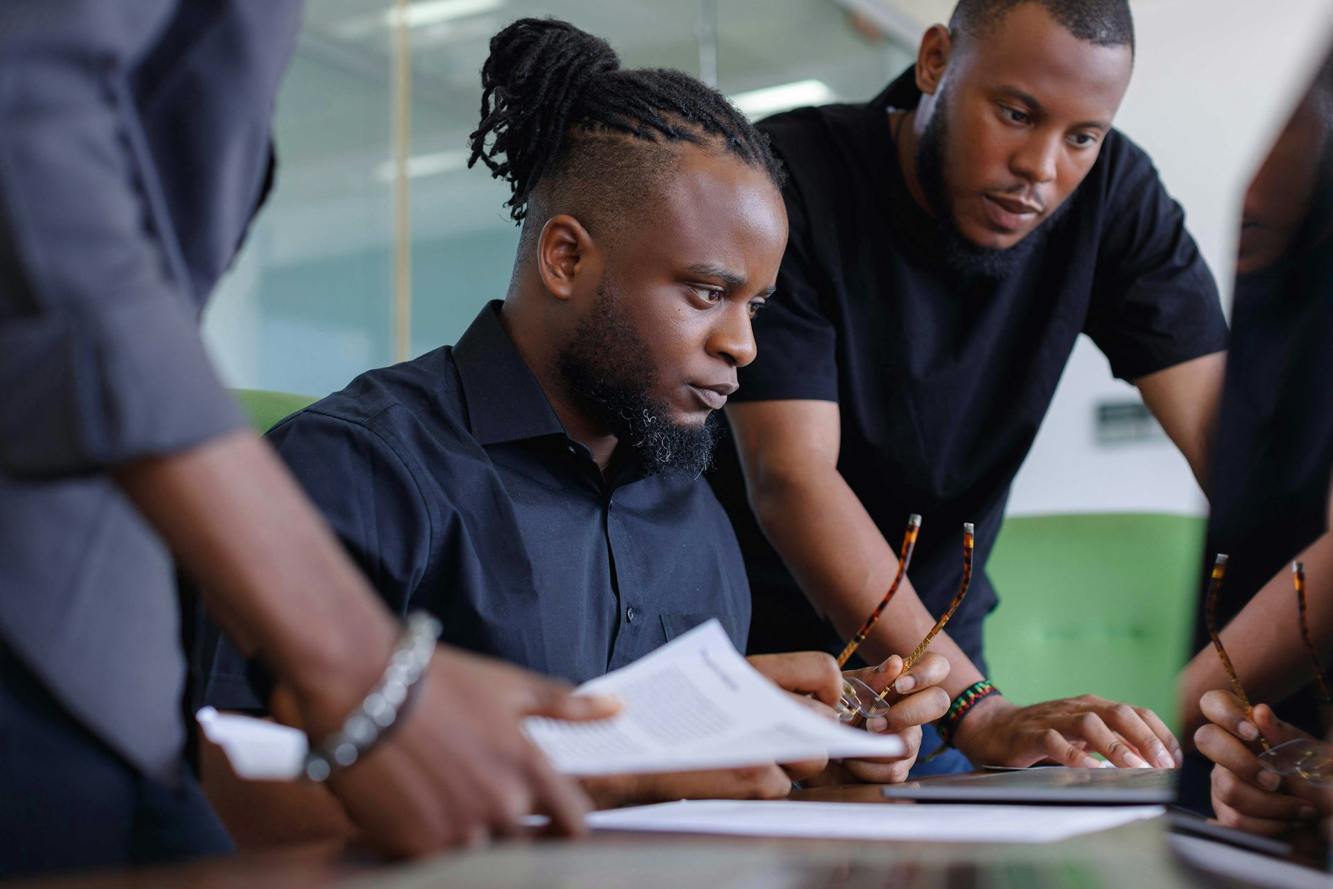 A group of young men gathered around a laptop in a workplace setting