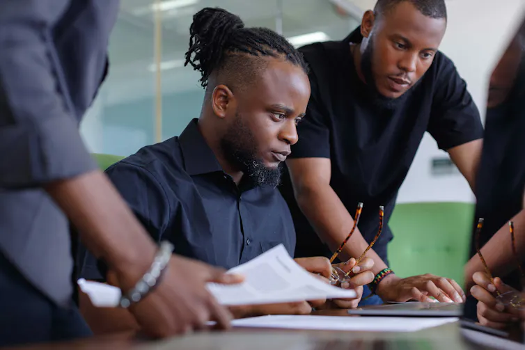 A group of young men gathered around a laptop in a workplace setting