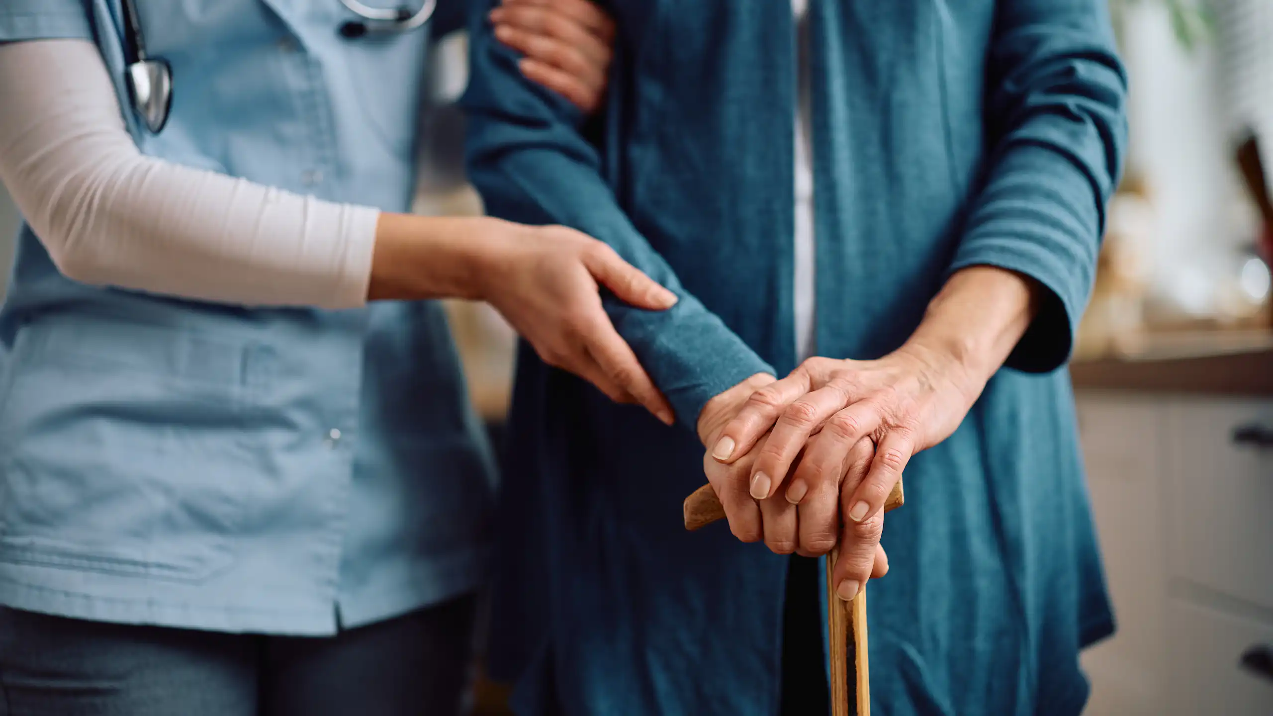 Close up of elderly person with walking cane and a nurse supporting.