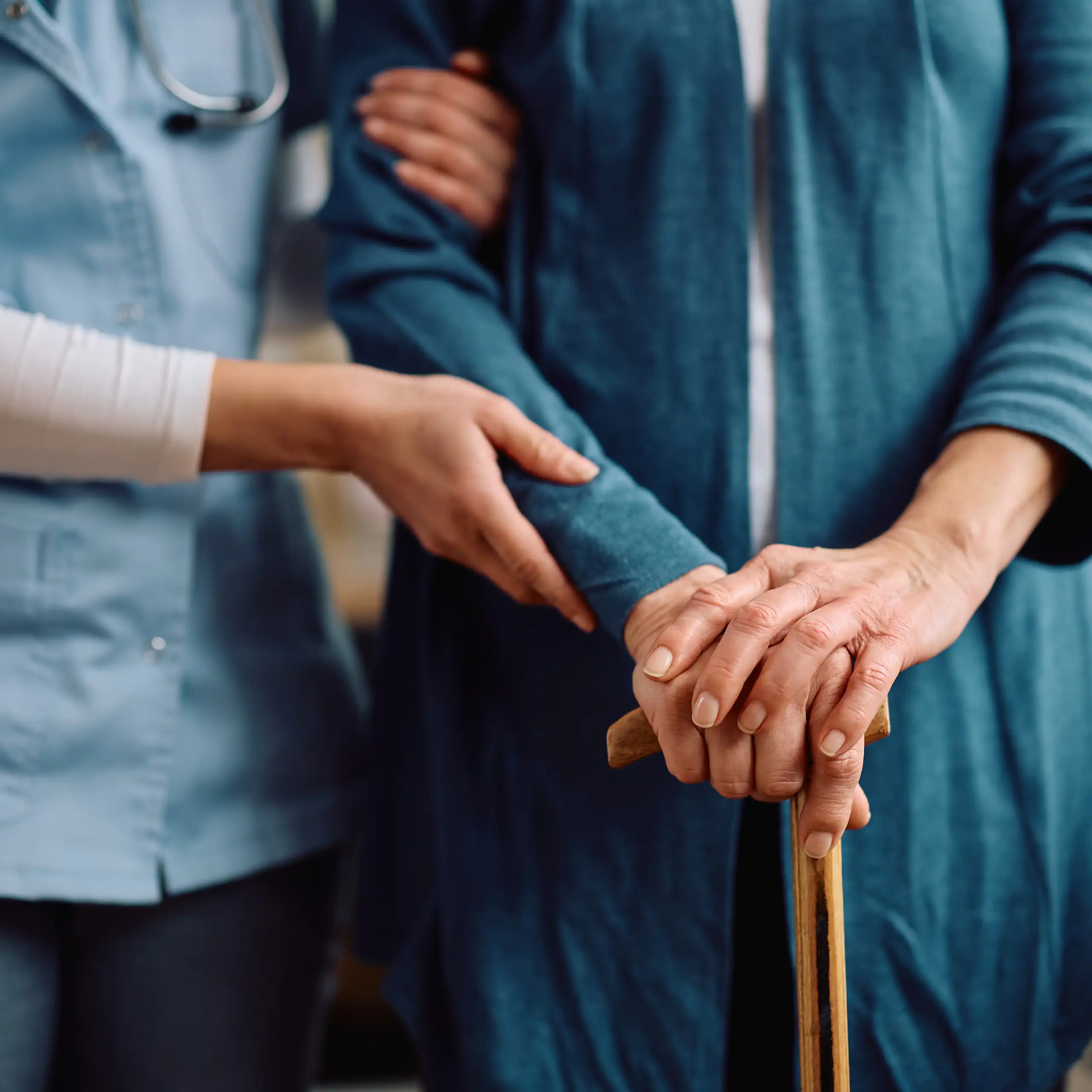 Close up of elderly person with walking cane and a nurse supporting.