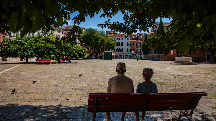 two people sitting on park bench in shade, heatwave.