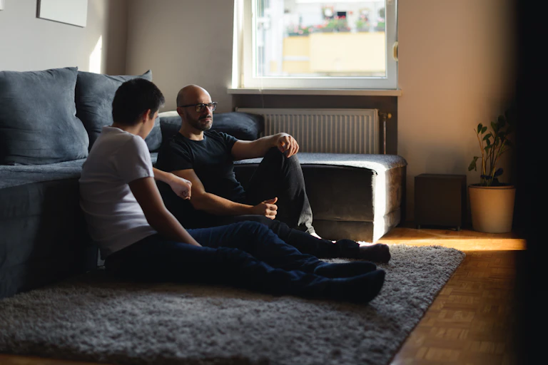 A father and his son talking on the floor of the living room.