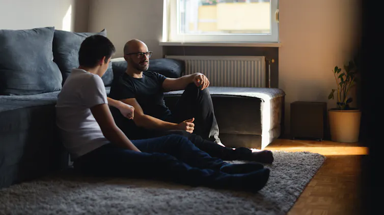 A father and his son talking on the floor of the living room.