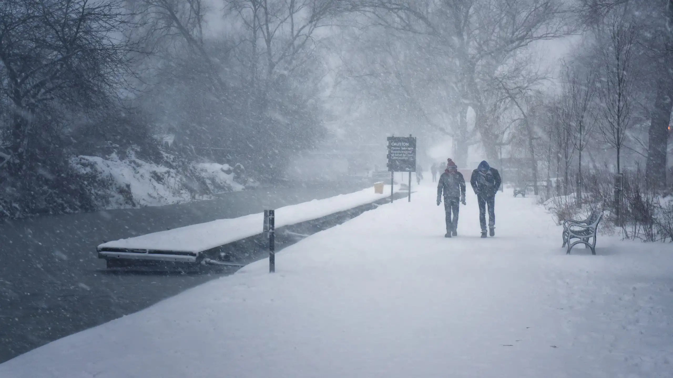 two people walk along snowy stormy canal