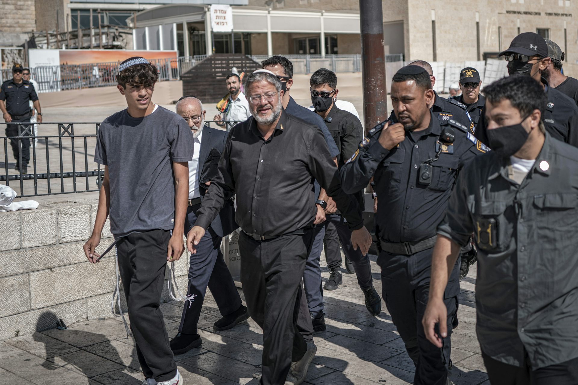 A man in black flanked by security personnel.