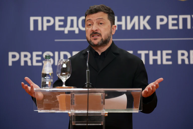 Portrait shot of Ukrainian president, Volodymyr Zelensky, at a podium with his hands held out.