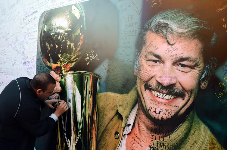 A man writes on a photo of another manwith a big mustache holding a trophy.
