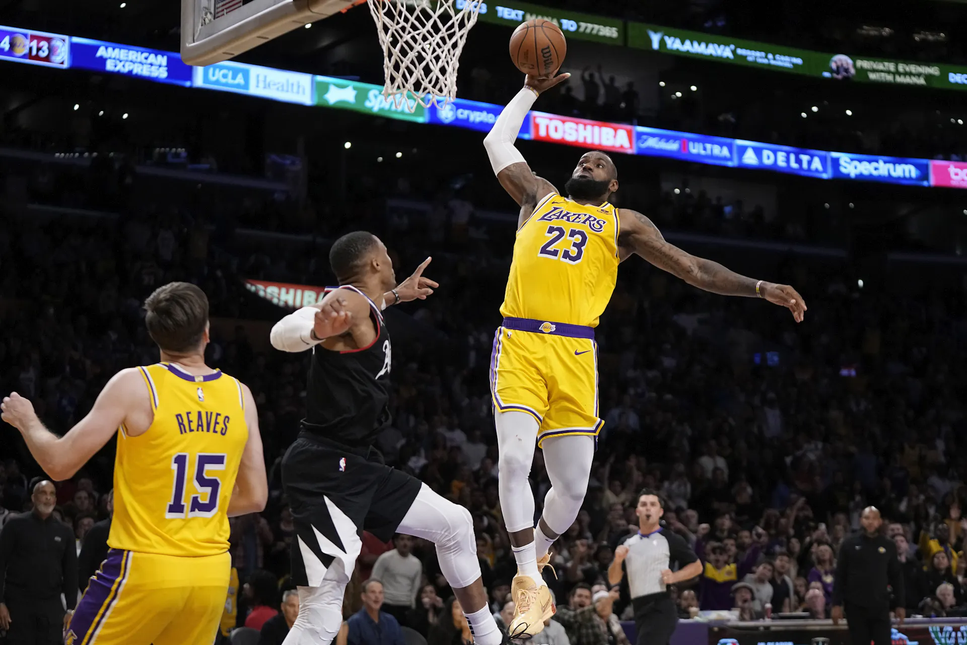 A basketball player in a yellow jersey prepares to dunk.