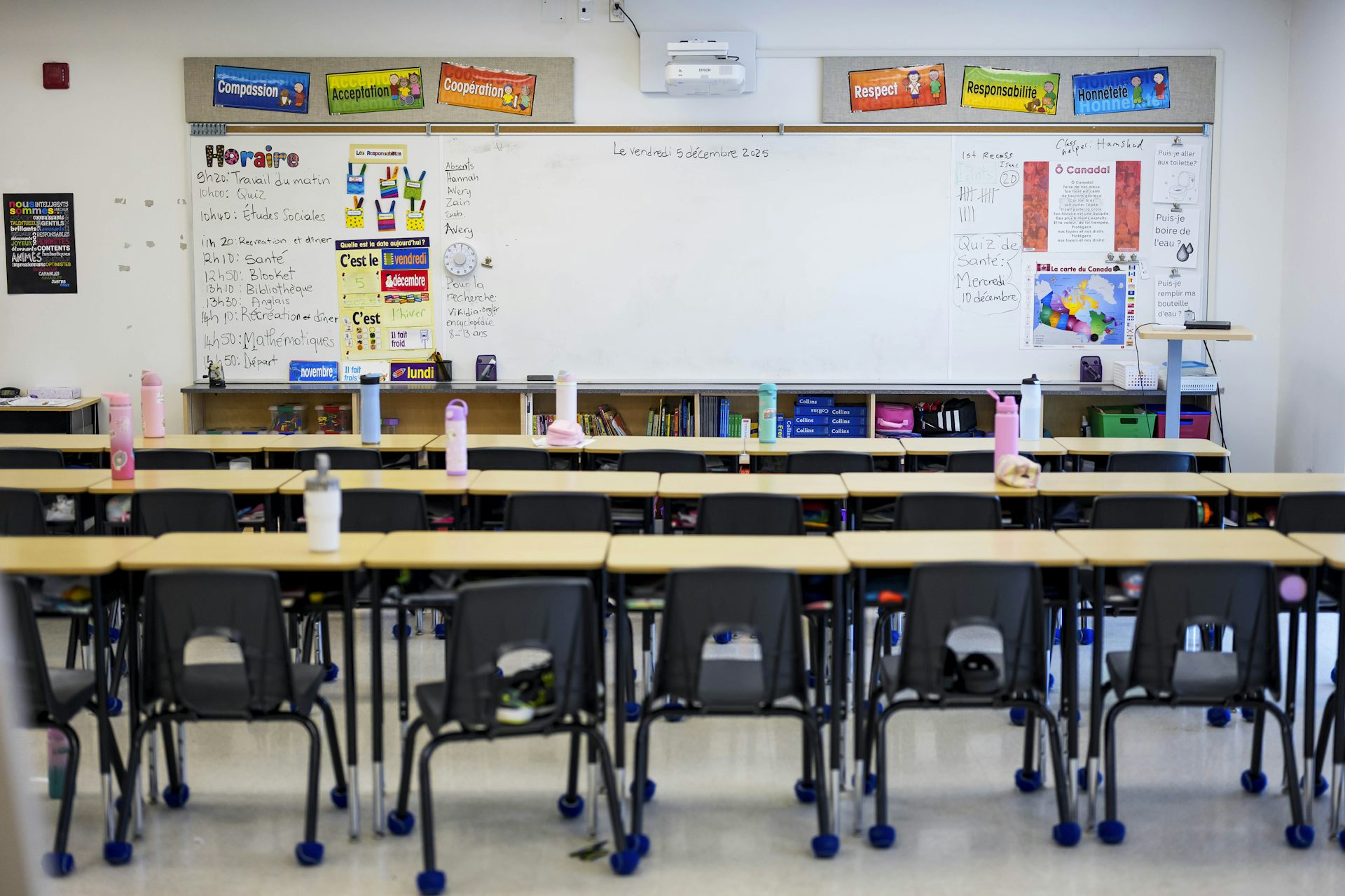 A classroom of desks in front of a white board and colourful decorated bulletin boards.