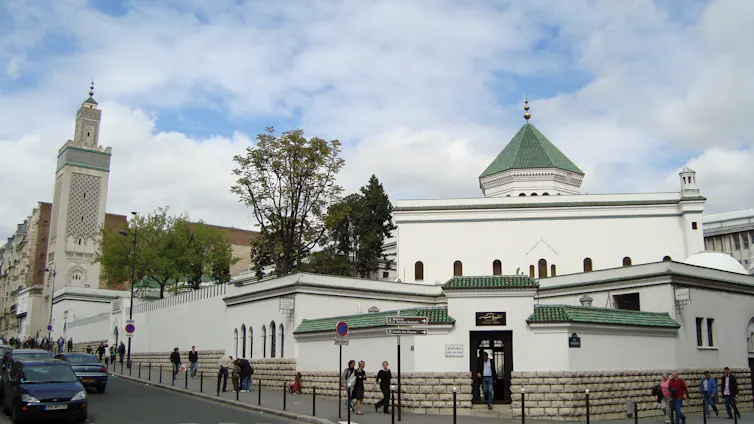 A large building with a green dome and tall minarets, with people walking in front of it.