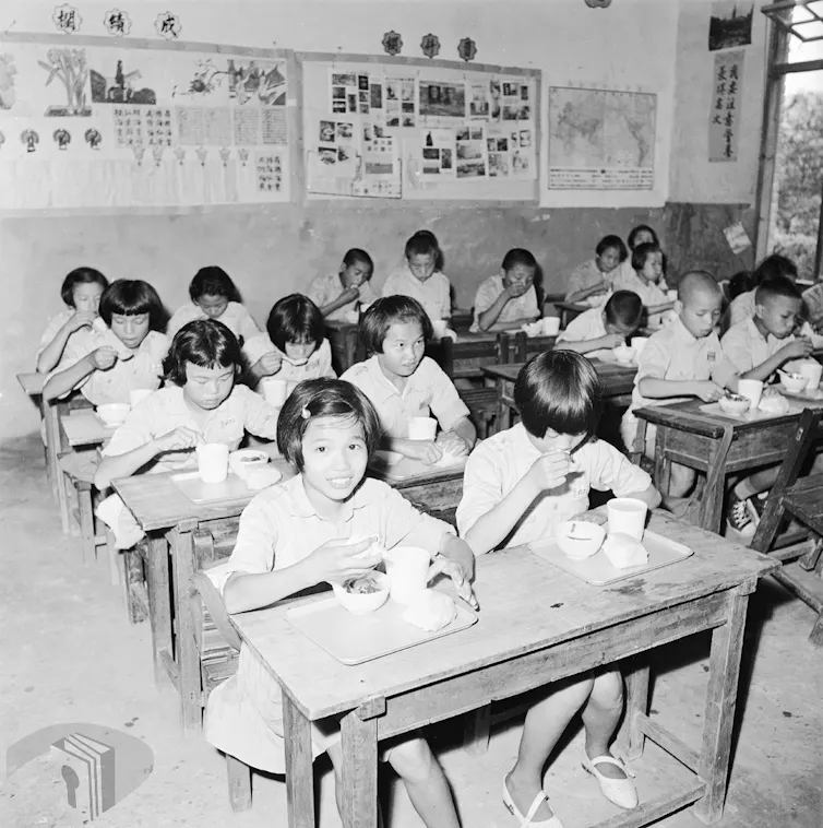 Black and white photo of children in uniform eating lunch at their desks