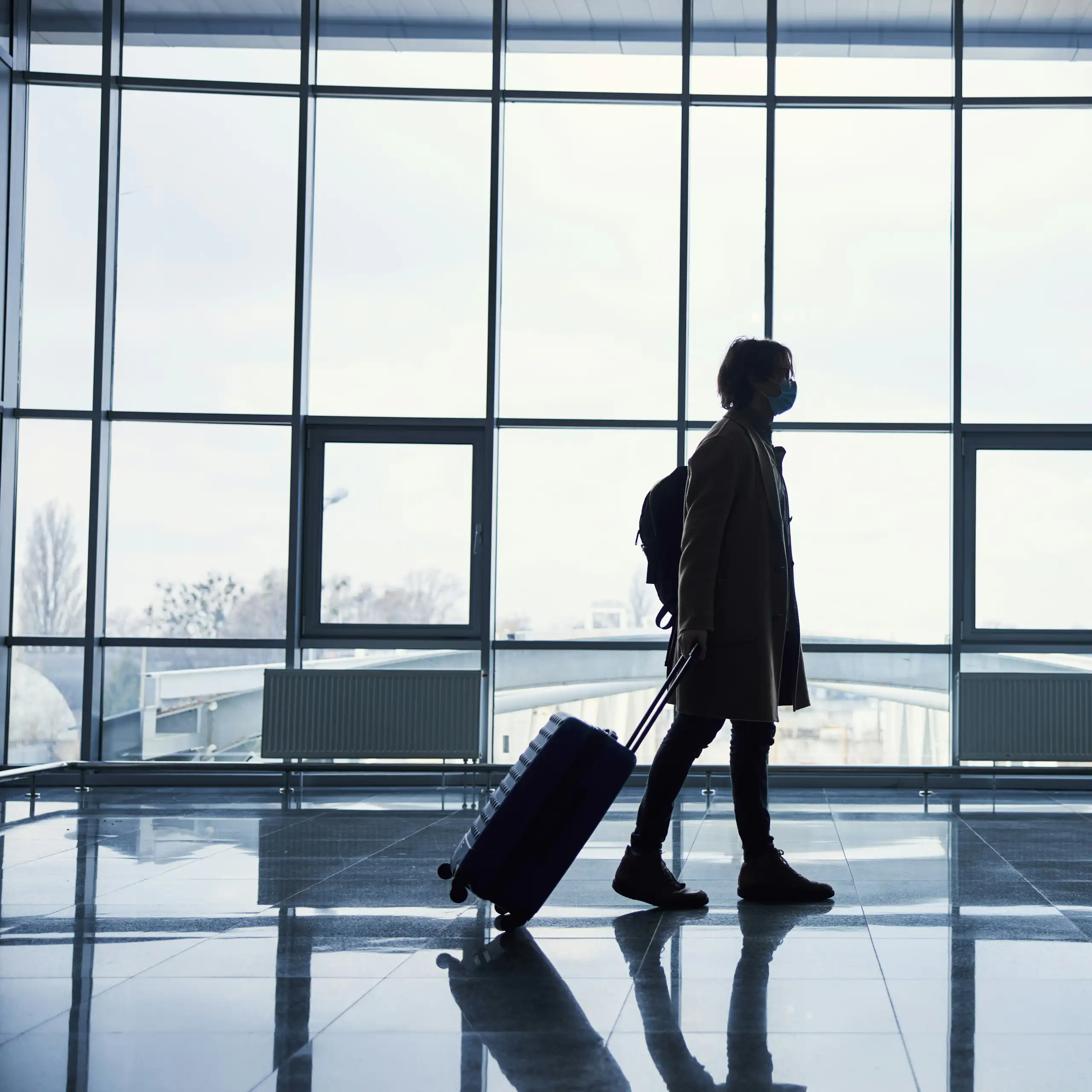 A silhouetted person in front of windows pulling a travel bag.