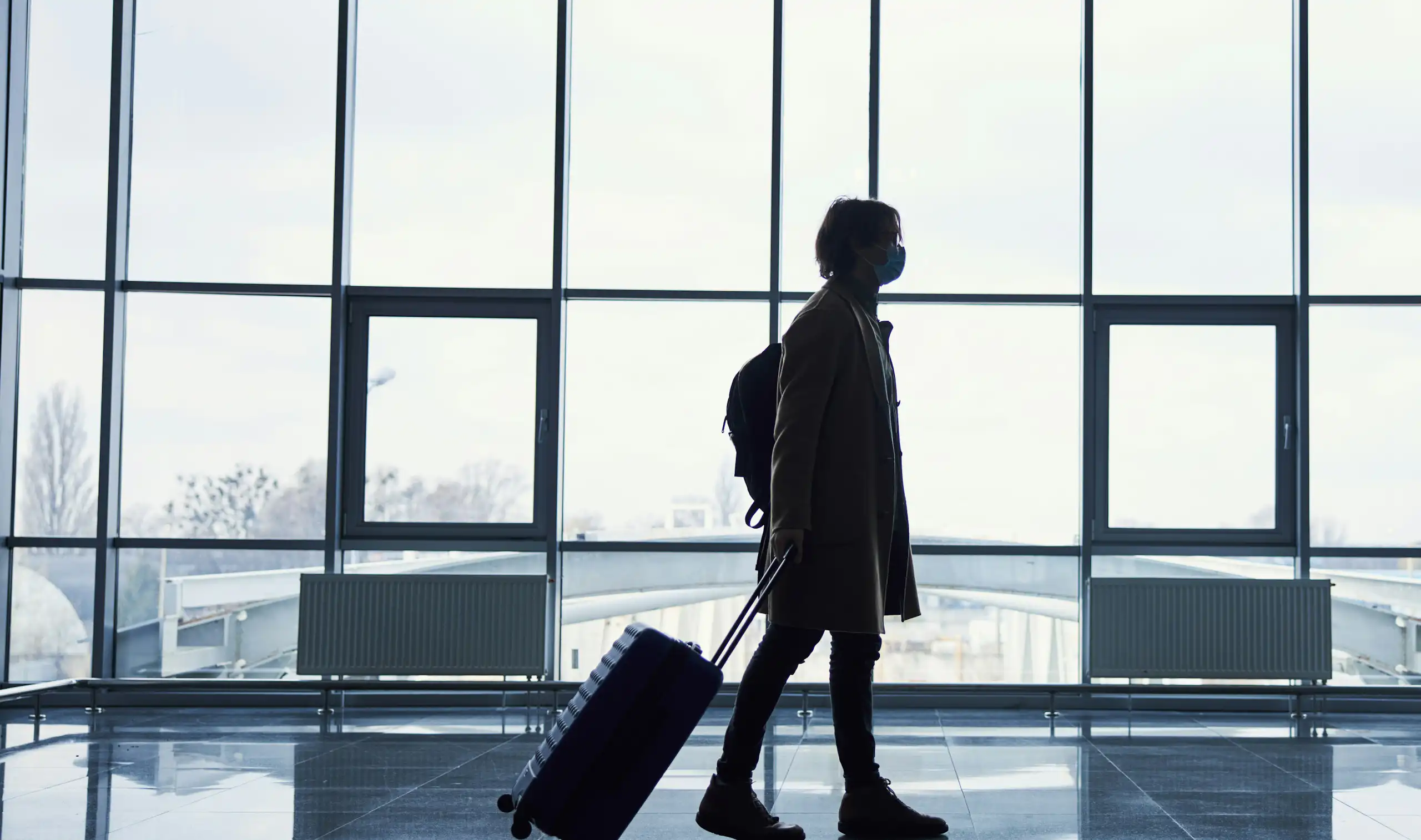 A silhouetted person in front of windows pulling a travel bag.