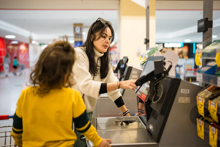 A woman paying at a supermarket checkout, watched by a child