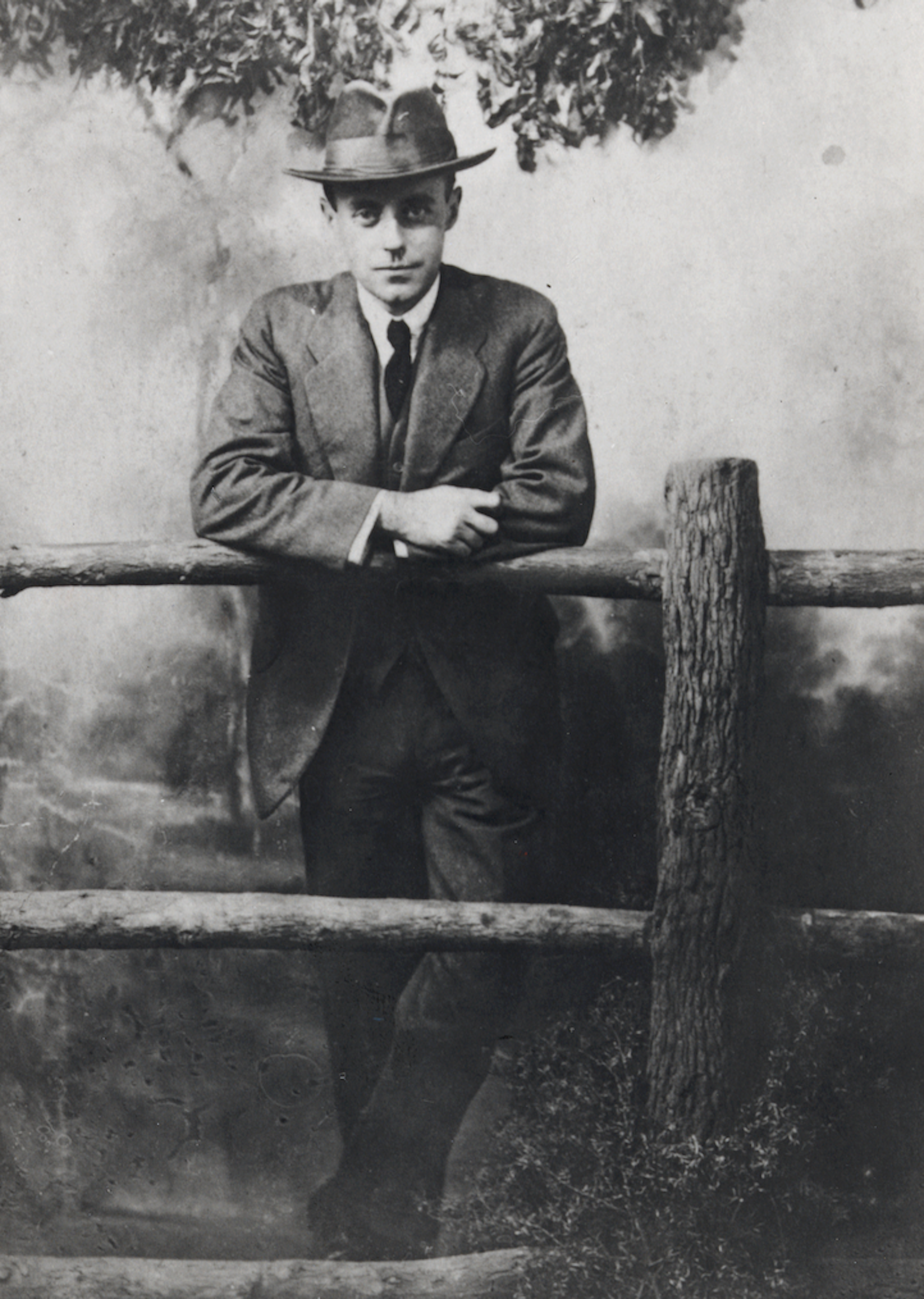 A man in a hat leaning on a wooden fence.