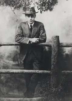 A man in a hat leaning on a wooden fence.