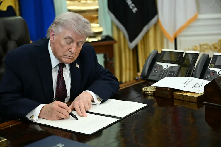 A man in a suit signs a document on his polished desk.