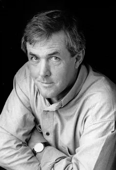 Don Watson, in a shirt, watch visible, smiling at the camera knowingly