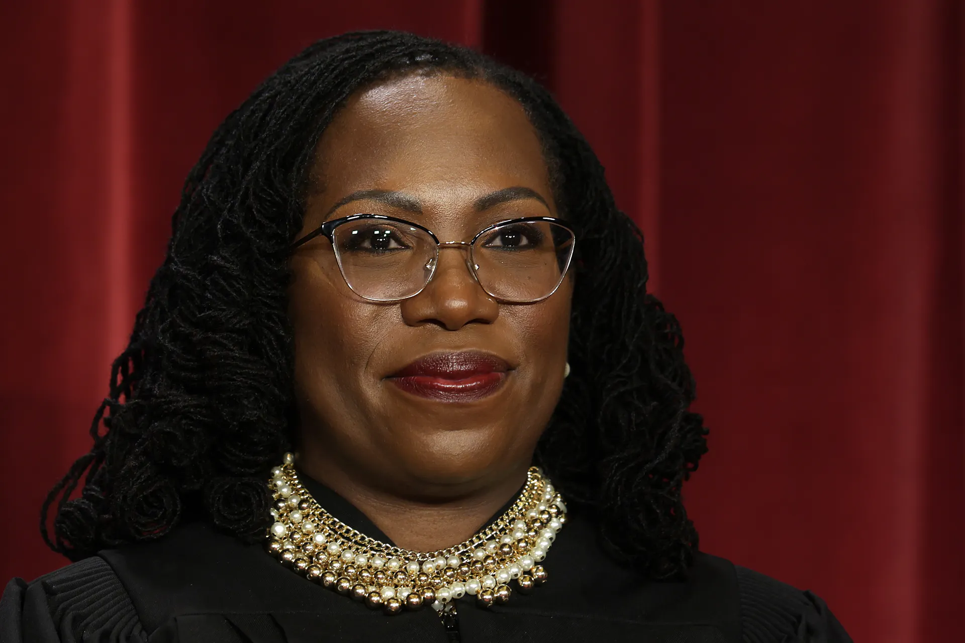 A young woman with black hair and wearing glasses and a black robe with white collar.