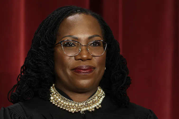 A young woman with black hair and wearing glasses and a black robe with white collar.