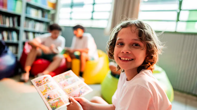 Young smiling boy reading a comic in the library.
