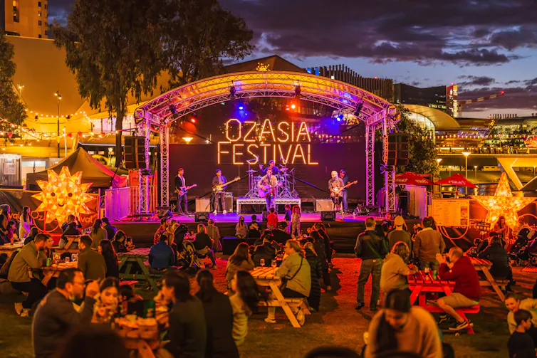 Front view of a stage at an arts festival, with tables full of people eating and chatting in front.