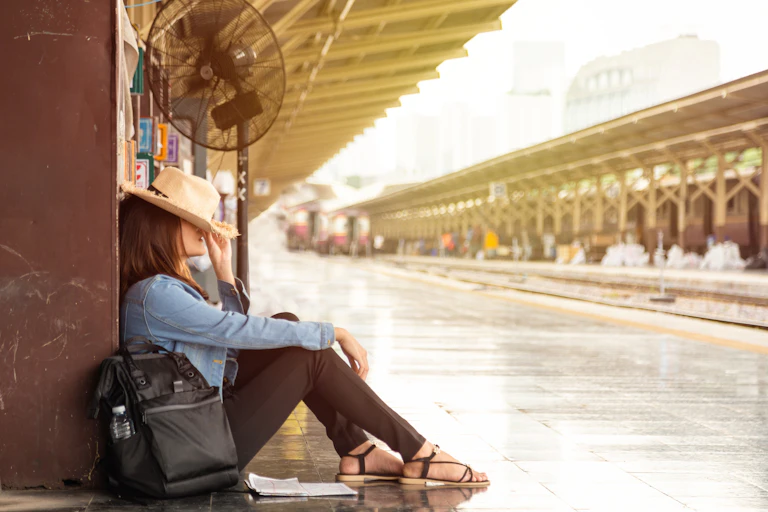 woman sat on train platform, straw hat on her face, hot, no trains