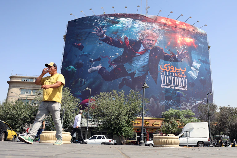 A man walks pas an anti-American billboard in Tehran, depicting US president Donald Trump drowning.