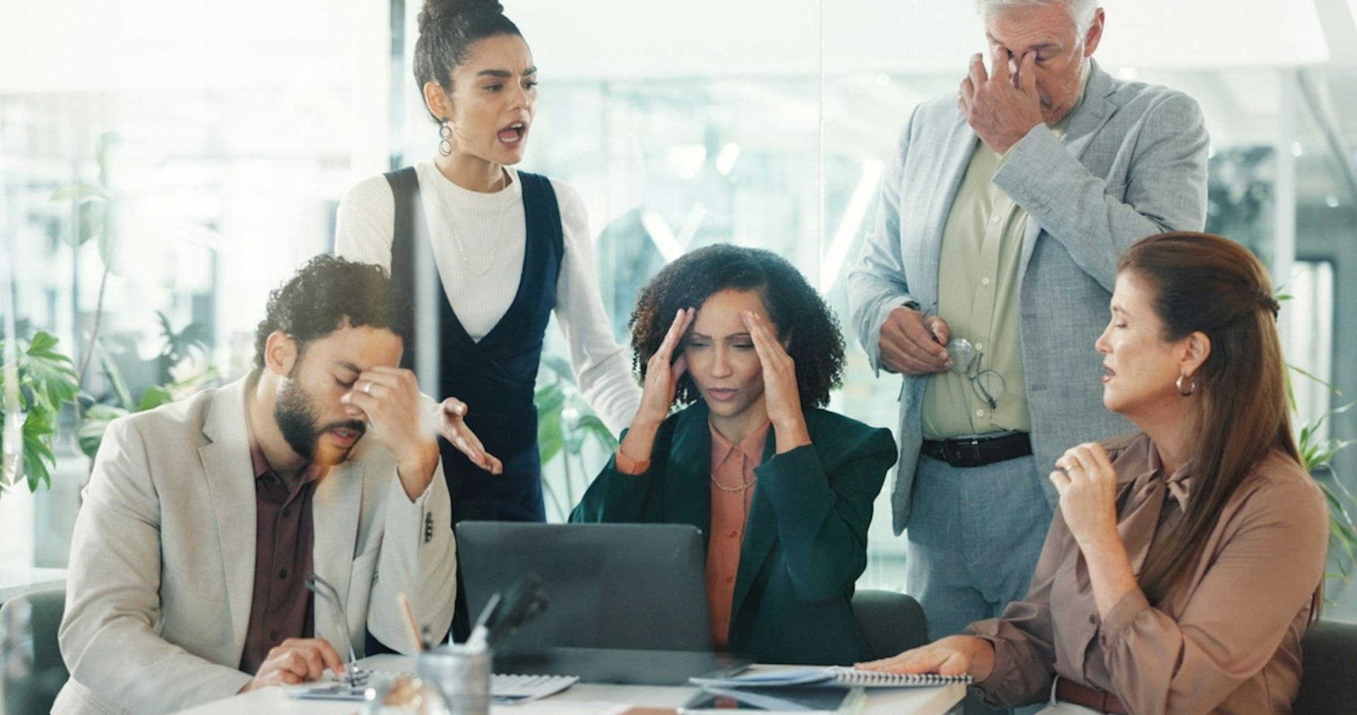 A group of stressed workers grouped around a laptop in an office
