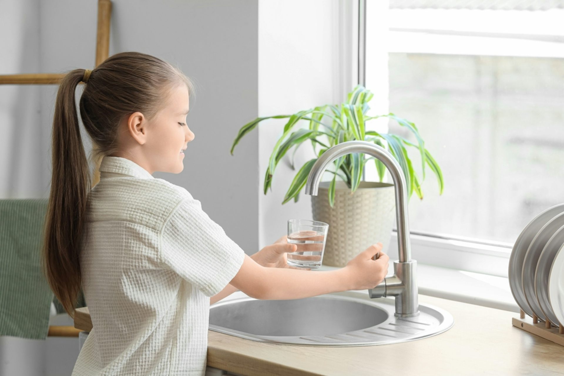 A girl fills a glass with water from a kitchen tap.