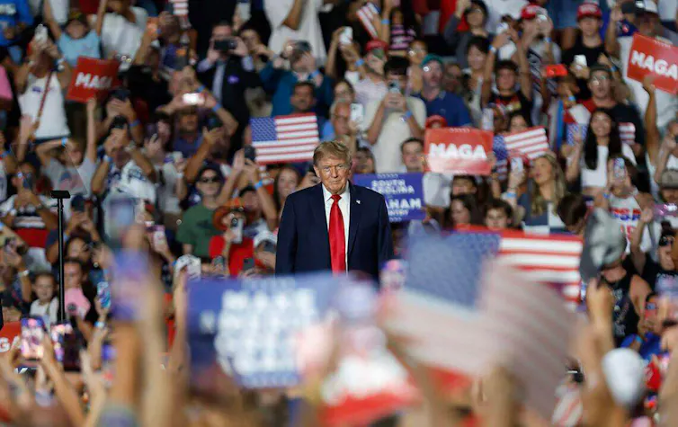 A man in a dark suit and red tie stands at the center of a packed Myrtle Beach Convention Center in Myrtle Beach, South Carolina, August 2026.