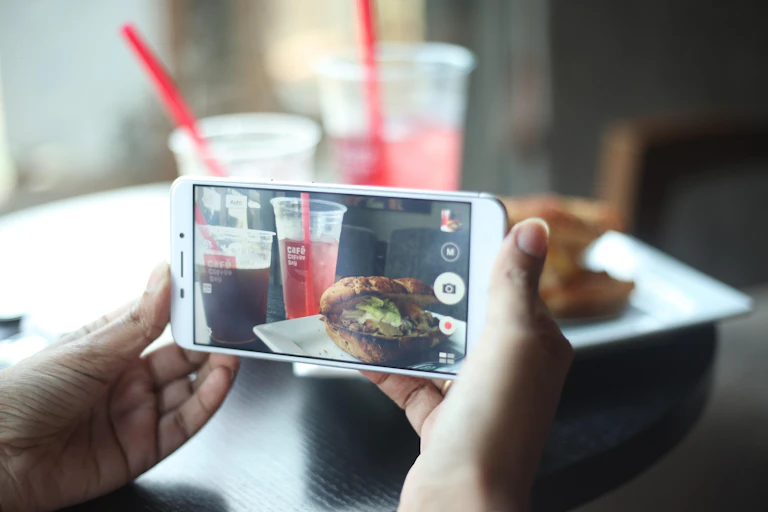 A mobile phone taking a photograph of a burger