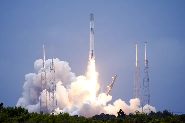 A rocket moving upwards off a launchpad, with a streak of flame and a plume of smoke coming off it.