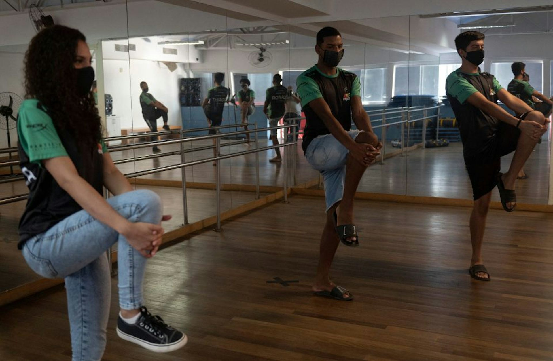 Two young men and one young woman balance on one leg while clasping the raised knee of their other leg with both hands.
