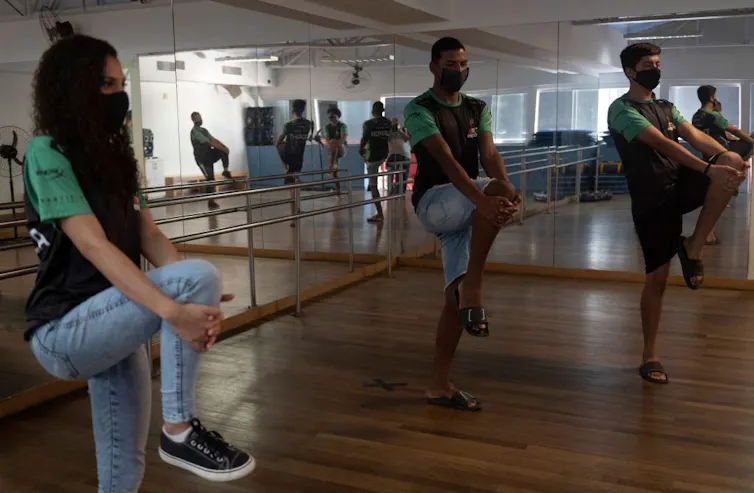 Two young men and one young woman balance on one leg while clasping the raised knee of their other leg with both hands.