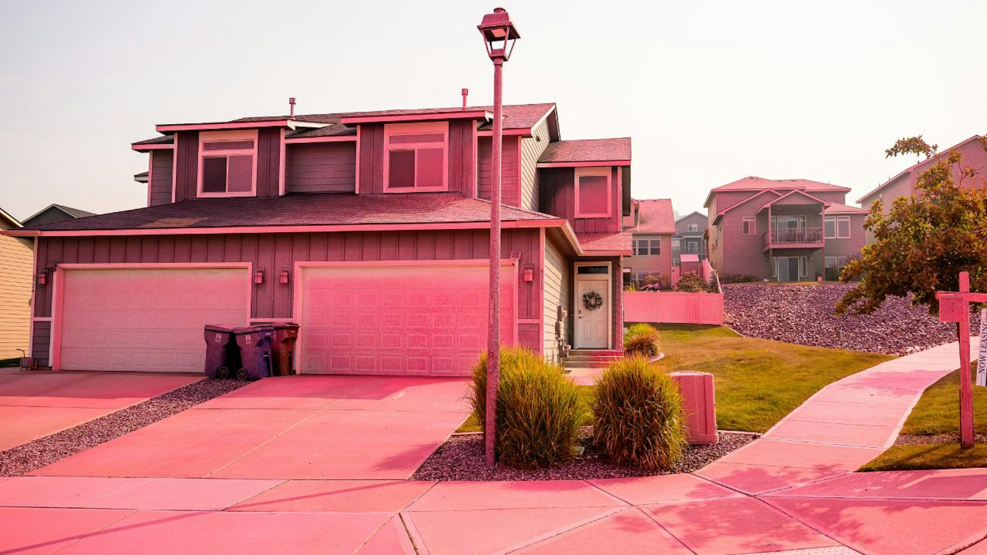 A house with a two-car garage in a neighborhood with several other homes. The driveway and walkways are paved and there is red fire retardant residue over everything.There is a tall lamp post in front of the house.