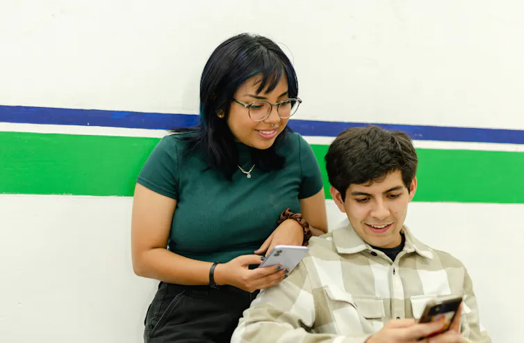 Two youth in front of a striped wall looking at a phone