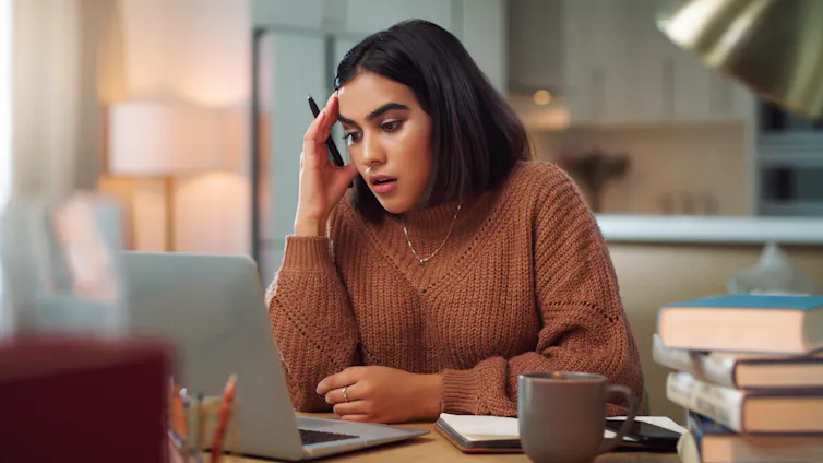 A young woman looking stressed out while using a laptop to study at home