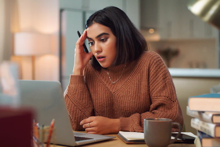 A young woman looking stressed out while using a laptop to study at home