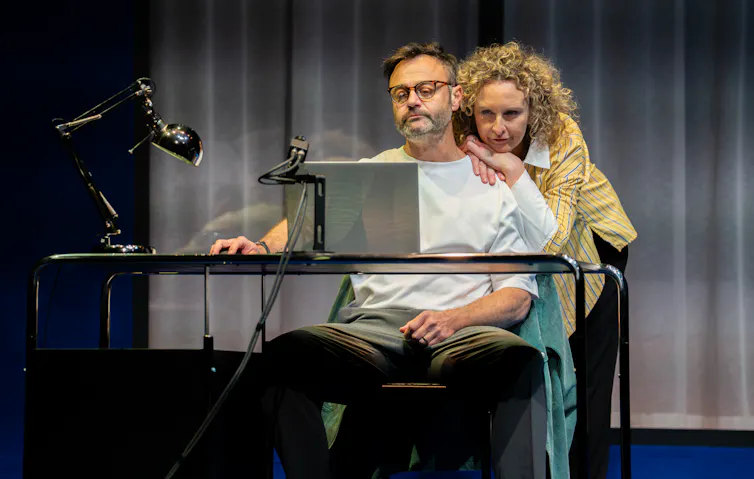 Production image: a man at a laptop, a woman leans on his shoulders.