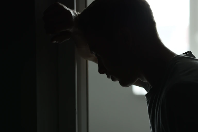 silhouette of a young man leaning his head against a wall