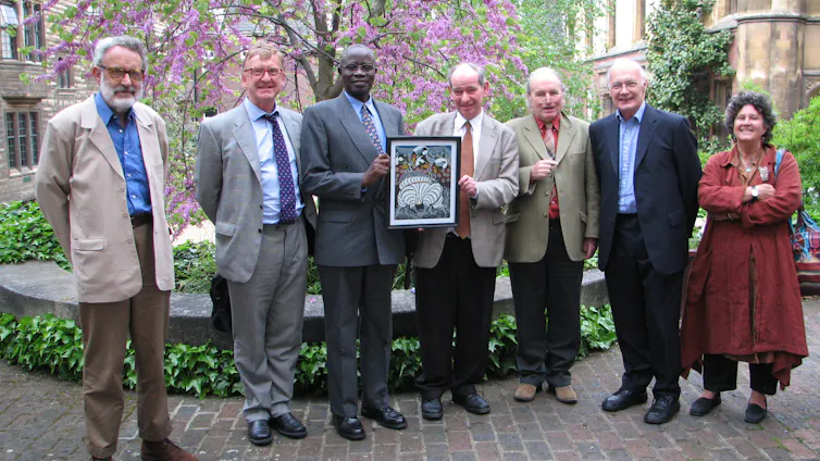 A man holding up a framed picture while standing in a line with six other people.