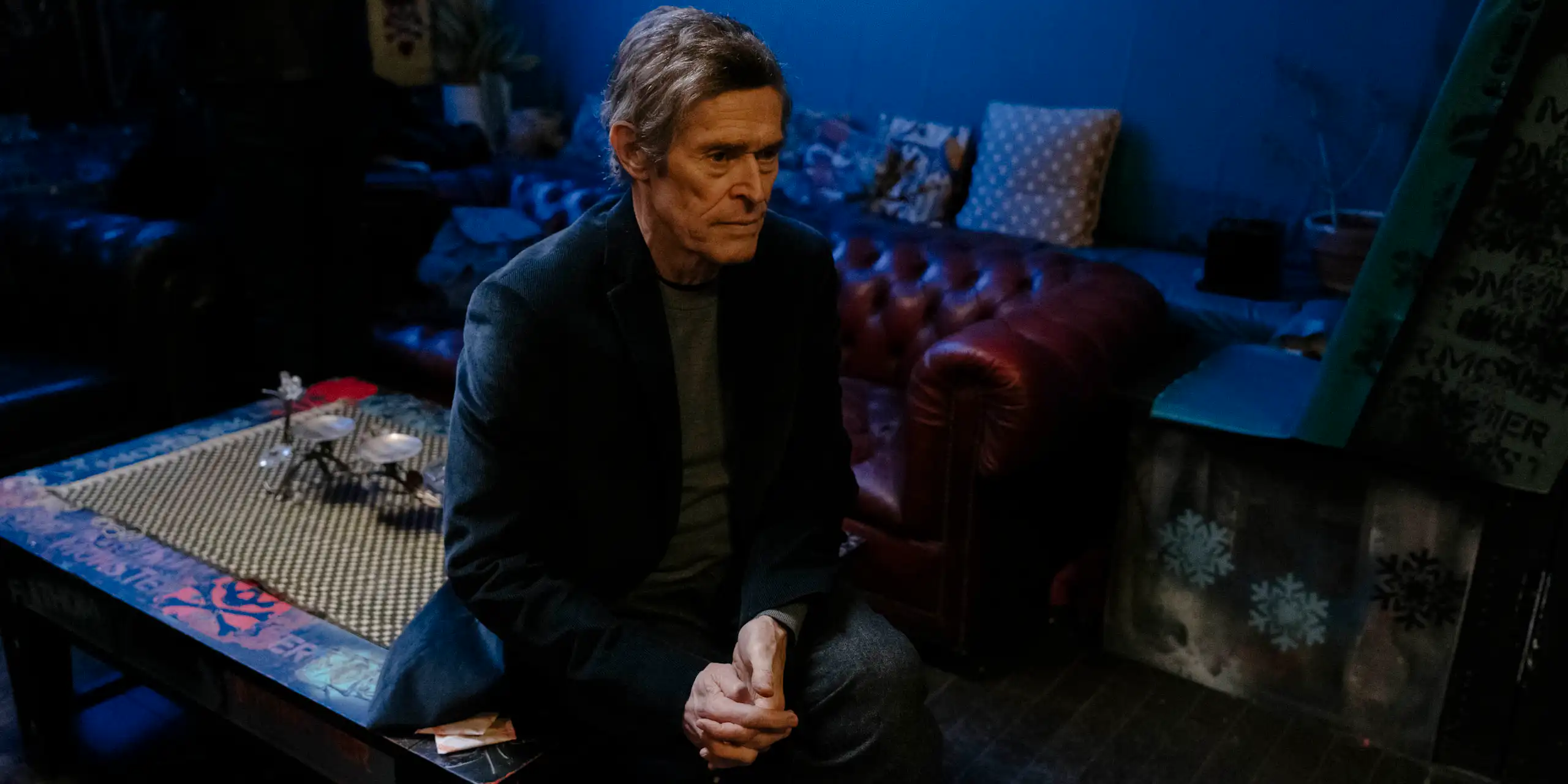 A man sitting in a blue-lit shadowy room looking pensive.