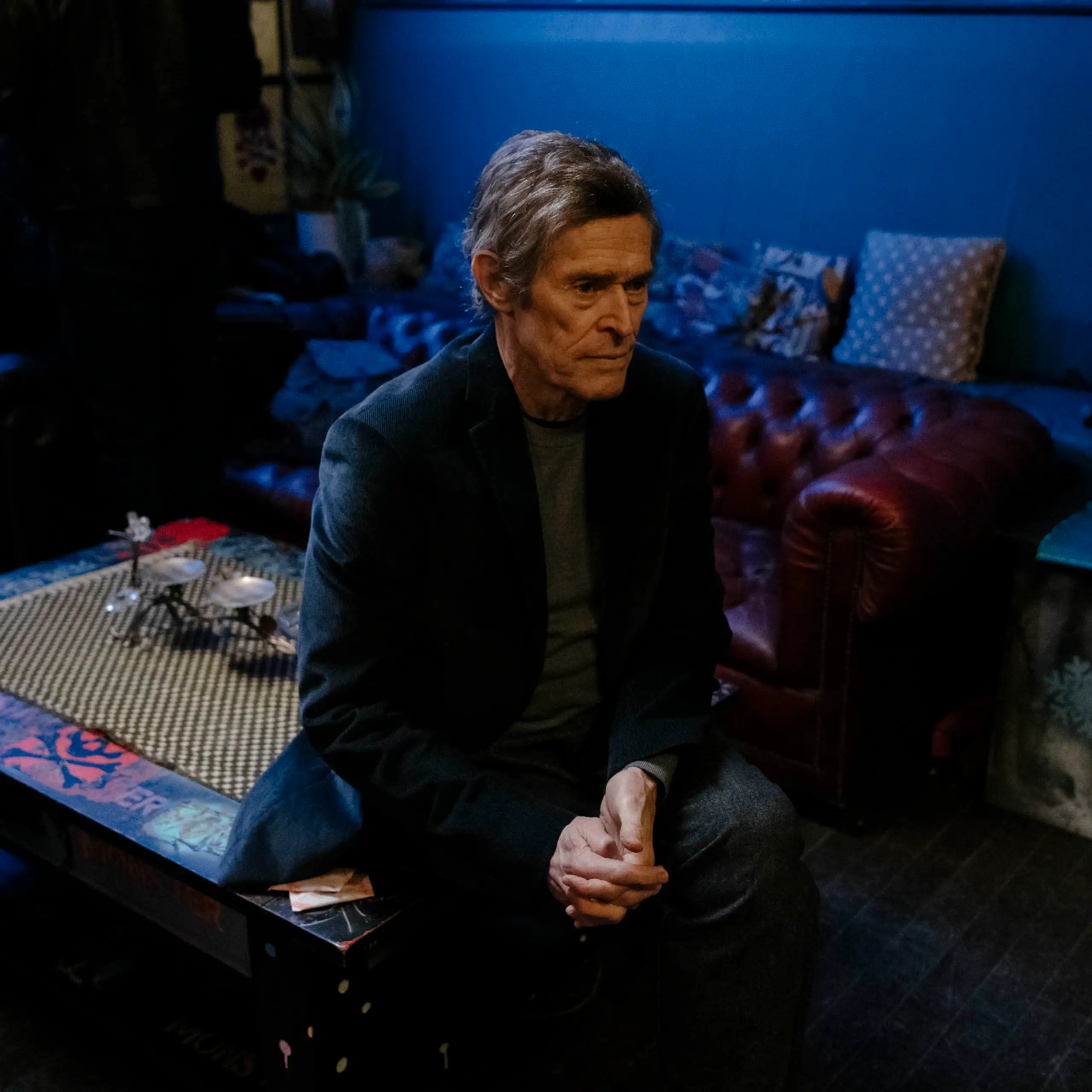 A man sitting in a blue-lit shadowy room looking pensive.
