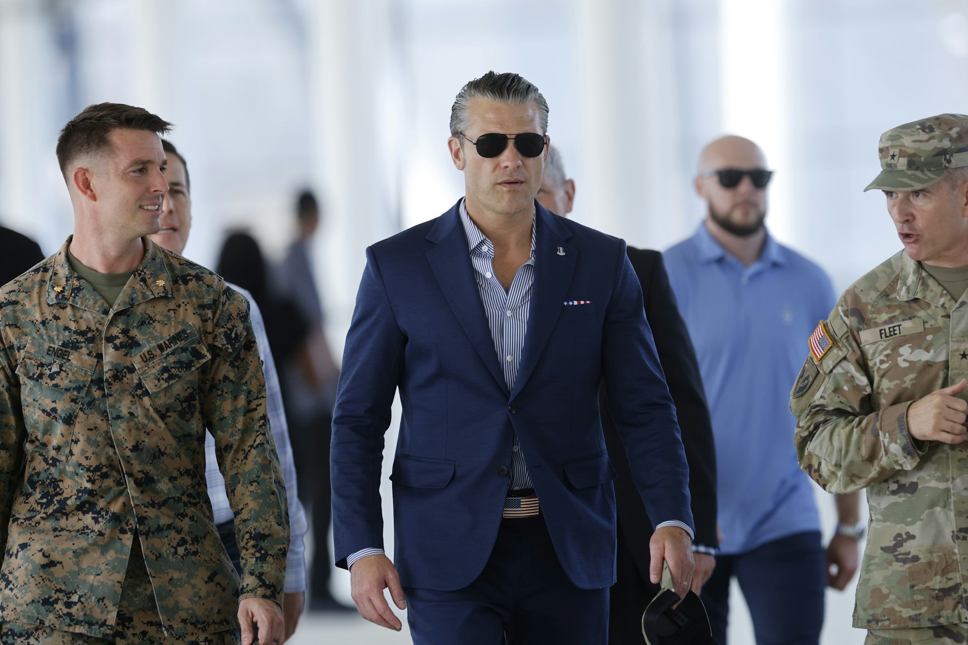 Pete Hegseth walks alongside two men in army attire.